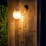 Applique murale extérieure en métal et verre avec globe transparent et bras courbé finition laiton