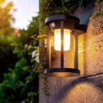 Applique murale extérieure noire en métal, forme lanterne avec diffuseur opalin, fixée sur mur en pierre