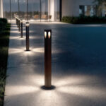 Balise sur pied cylindrique en métal finition rouille, ouverture latérale laissant émettre un éclairage doux au sol