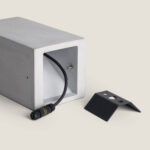 Balise extérieure en ciment rectangulaire grise, ouverture arrière avec câble et connecteur, socle de fixation métallique noir