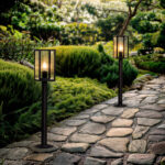 Balise sur pied noire en métal, lanterne vitrée diffusant lumière chaude le long d'un chemin pavé