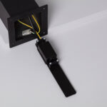 Balise extérieure sur pied noire, corps métallique, base carrée ouverte montrant câblage et support de fixation