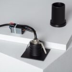 Balise encastrable murale noire avec corps cylindrique et platine carrée, câbles et transformateur visibles