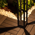 Balise sur pied noire en métal à fentes verticales éclairant terrasse en bois