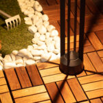 Balise sur pied extérieure noire en métal avec fût cylindrique et barres verticales sur terrasse en bois