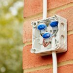 Connecteurs IDC bleus dans boîtier étanche blanc fixé sur brique, câbles extérieurs raccordés