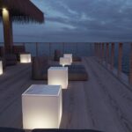 Lampe cube blanche lumineuse posée sur terrasse en bois au bord de l'eau