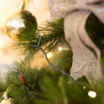 Guirlande LED blanc chaud câble vert foncé sur branche de sapin décorée d'une boule dorée