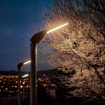 Lampadaire LED sur mât gris métal, tête plate allongée émettant lumière chaude pour éclairage extérieur