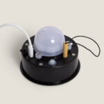 Tête de lampe LED avec diffuseur blanc opalin, base noire circulaire et petite batterie cylindrique jaune