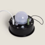 Module LED avec diffuseur dôme sur base circulaire noire, batterie cylindrique verte et câbles visibles