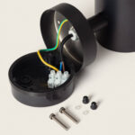 Lampe murale extérieure noire cylindrique avec boîtier de raccordement ouvert, câbles et vis de fixation visibles