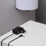 Lampe murale cylindrique blanche fixée au mur, chargeur secteur noir et câbles de recharge sur surface