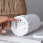 Lampe à poser blanche cylindrique avec corde naturelle tressée, compartiment à piles visible et interrupteur