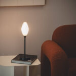 Lampe à poser LED à abat-jour ovale blanc, pied noir, sur table près d'un fauteuil marron