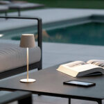 Lampe à poser beige avec abat-jour tissu et pied métallique mince, posée sur table d'extérieur