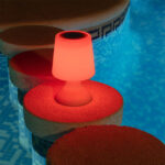 Lampe à poser LED portable en plastique opaque, forme conique, éclairage rouge posée sur margelle de piscine