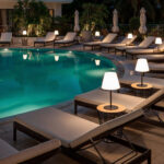 Lampe à poser LED blanche sur pied noir, posée sur table près d'une piscine extérieure la nuit