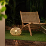 Lampe à poser rotin tressé ronde, lumière chaude, style lanterne, posée sur pelouse extérieure