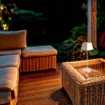 Lampe à poser LED beige en aluminium, abat-jour carré, pied fin, posée sur table d'extérieur en osier