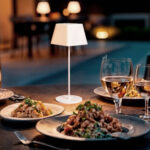 Lampe à poser blanche au pied fin et abat-jour carré, posée sur table extérieure