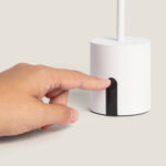 Lampe à poser blanche base cylindrique avec commande tactile noire, tige fine, main appuyant sur le bouton