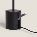 Lampe à poser noire cylindrique avec tige, port de charge USB visible et câble branché