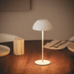 Lampe à poser blanche, abat-jour dôme mat, pied fin et base ronde posée sur table en bois