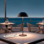 Lampe à poser noire sur pied fin, abat-jour en demi-sphère et base ronde, posée sur table extérieure