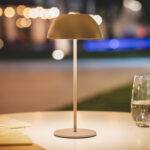 Lampe à poser taupe, abat-jour arrondi, pied fin et socle rond, posée sur table