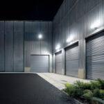 Projecteur LED mural blanc froid installé sur façade métallique, éclairage extérieur de portes sectionnelles