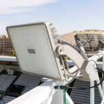 Projecteur LED rectangulaire gris monté sur support orientable avec dissipateurs, câblage apparent pour éclairage extérieur de stade