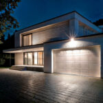 Projecteur LED extérieur blanc fixé au-dessus d'un garage éclairant l'allée