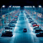 Projecteur LED extérieur monté sur mât, lumière blanc froid, corps rectangulaire, éclaire grand parking nocturne