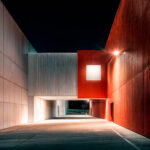 Projecteur LED mural fixé sur façade rouge, lumière blanche directionnelle illuminant passage extérieur nocturne