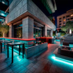 Ruban LED RGB extérieur posé en bandes cyan et rouge le long de mobilier et marches