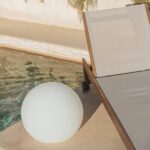 Lampe sphérique blanche posée au sol près d'une piscine