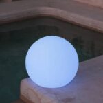 Lampe à poser sphérique émettant une lumière bleu froid, posée au bord d'une piscine