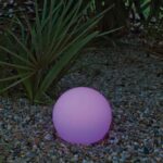 Lampe sphérique LED rose-violet, finition mate, posée au sol sur gravier pour éclairage extérieur