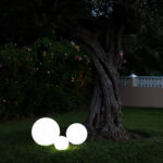 Trois sphères LED blanches rechargeables posées sur la pelouse près d'un arbre