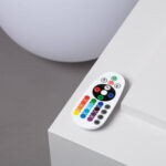 Télécommande blanche à boutons colorés, à côté d'une lampe sphérique LED blanche