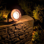 Spot extérieur circulaire aluminium noir sur piquet, orientable, fixé sur muret en pierre