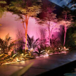 Wallwasher mural illuminant la façade et végétation en tons rose amarante, lumière directionnelle basse