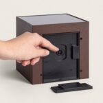 Applique murale solaire cubique en aluminium brun, panneau solaire dessus et trappe arrière ouverte avec main manipulant le boîtier