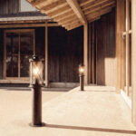 Balise sur pied cylindrique en acier inoxydable, finition sombre, lanterne à verre et support grillagé pour éclairage extérieur